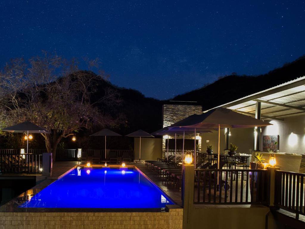 a swimming pool at night with tables and umbrellas at Shepherds Tree Game Reserve in Pilanesberg