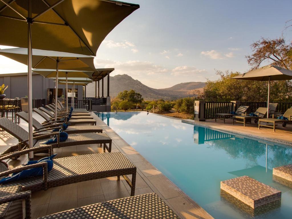 a swimming pool with lounge chairs and umbrellas at Shepherds Tree Game Reserve in Pilanesberg