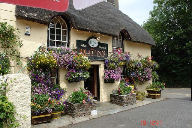 uma velha pousada com muitas flores em frente em The Old Inn em Mullion