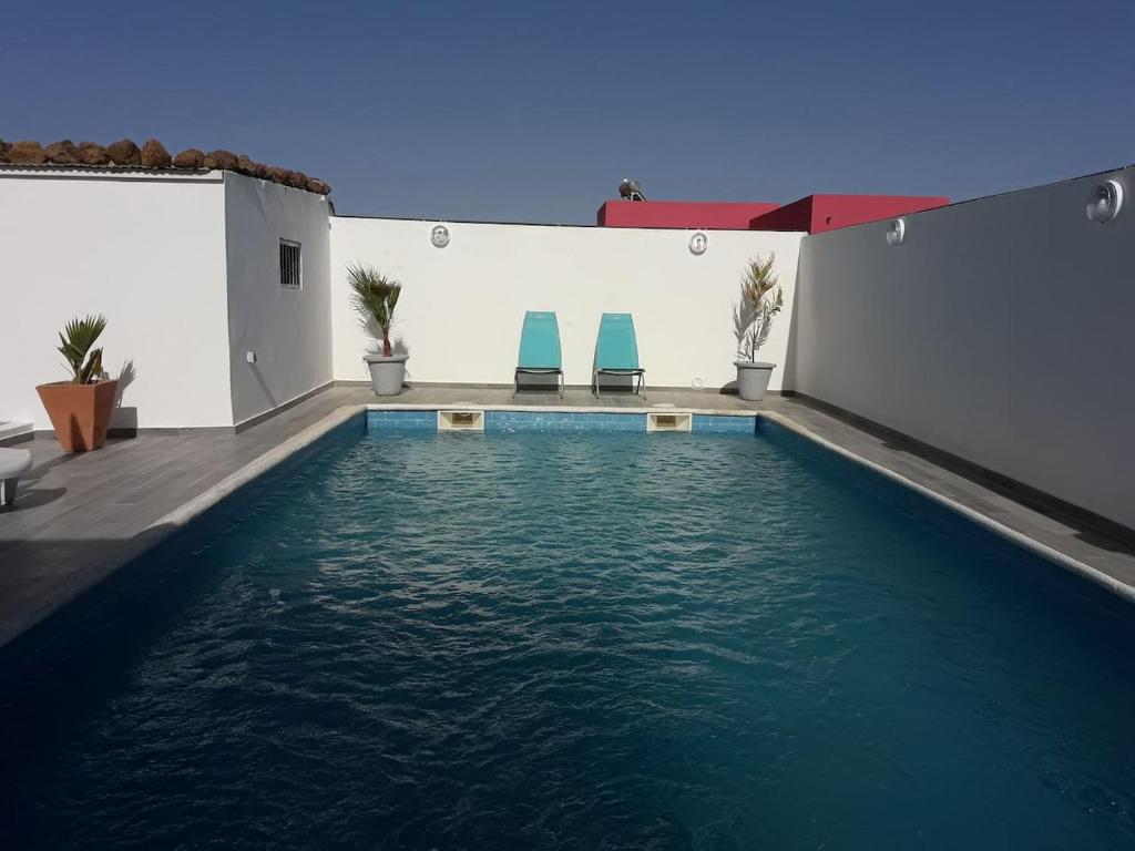 una piscina con 2 sillas azules junto a un edificio en African Jaja villa Piscine-Climatisation en Poponguine