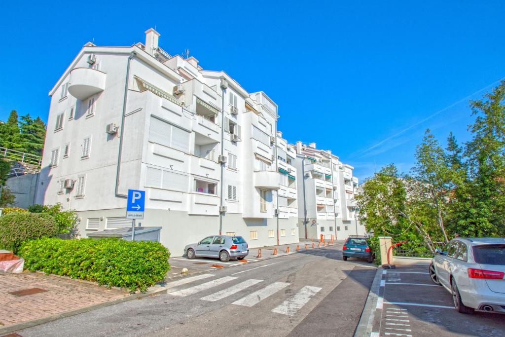 un grand bâtiment blanc avec des voitures garées dans un parking dans l'établissement Apartment Ruzica, à Crikvenica