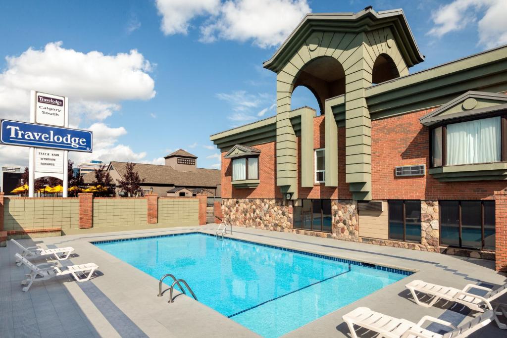 a swimming pool in front of a building with chairs at Travelodge by Wyndham Calgary South in Calgary