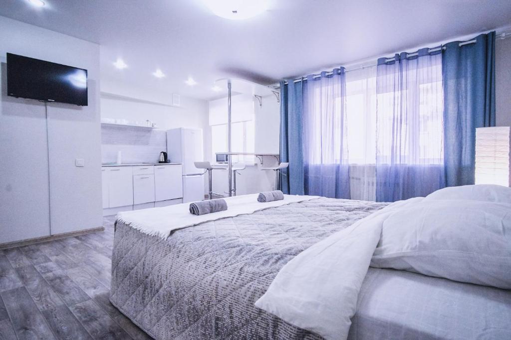 a white bedroom with a large bed and a television at Отличная студия в центре Красноярска, район ЖД вокзала in Krasnoyarsk