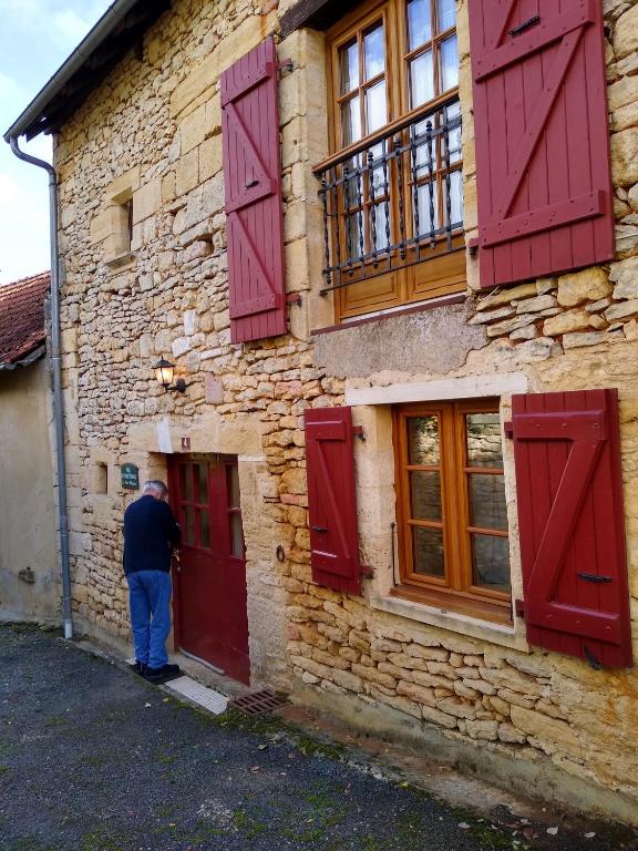 un homme debout à l'extérieur d'un bâtiment avec des portes rouges dans l'établissement Little House in the Dordogne, à Salignac Eyvigues