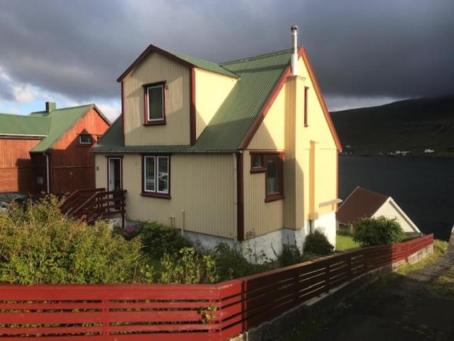 ein gelbes Haus mit einem grünen Dach und einem roten Zaun in der Unterkunft Det lille gule hus in Trongisvágur