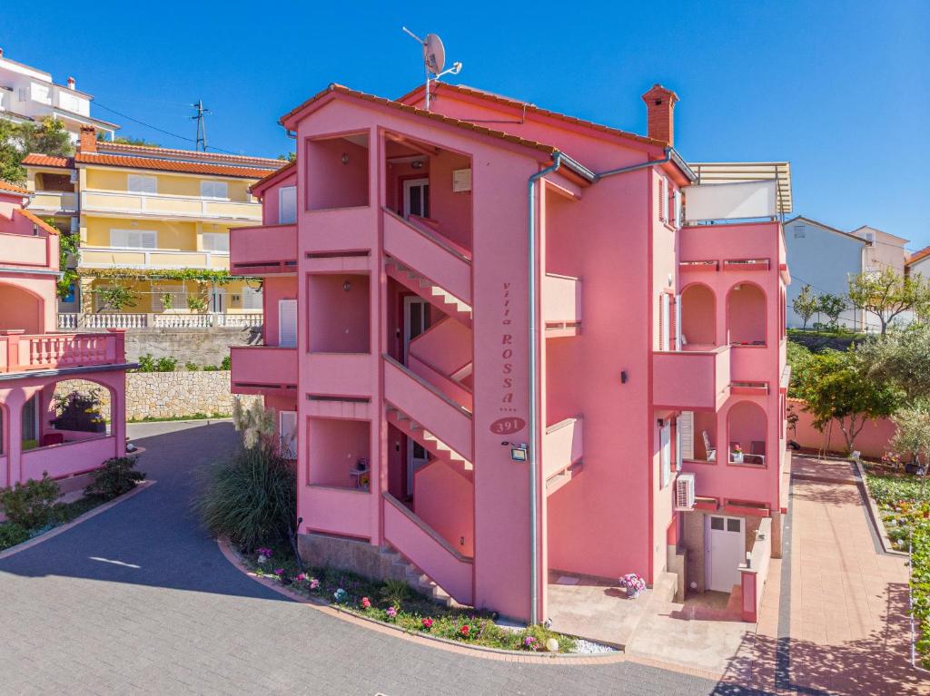 a pink building with a red roof at Villa Rossa Apartments in Rab