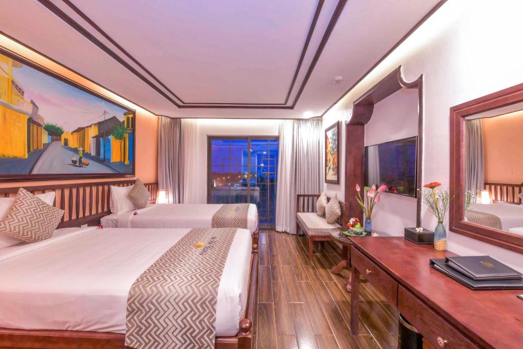 a hotel room with two beds and a desk at Fivitel Hoi An Hotel in Hoi An