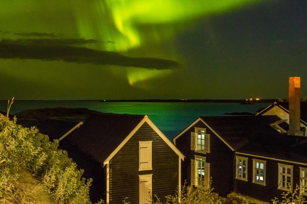 une image de l'aurore dansant dans le ciel au-dessus des maisons dans l'établissement Englendingavík Homestay, à Borgarnes