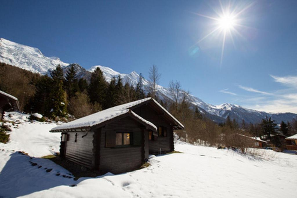 シャモニー・モンブランにあるChalet du Glacier - Happy Rentalsの雪の中の小さな木造キャビンで、太陽が背後に沈みます。
