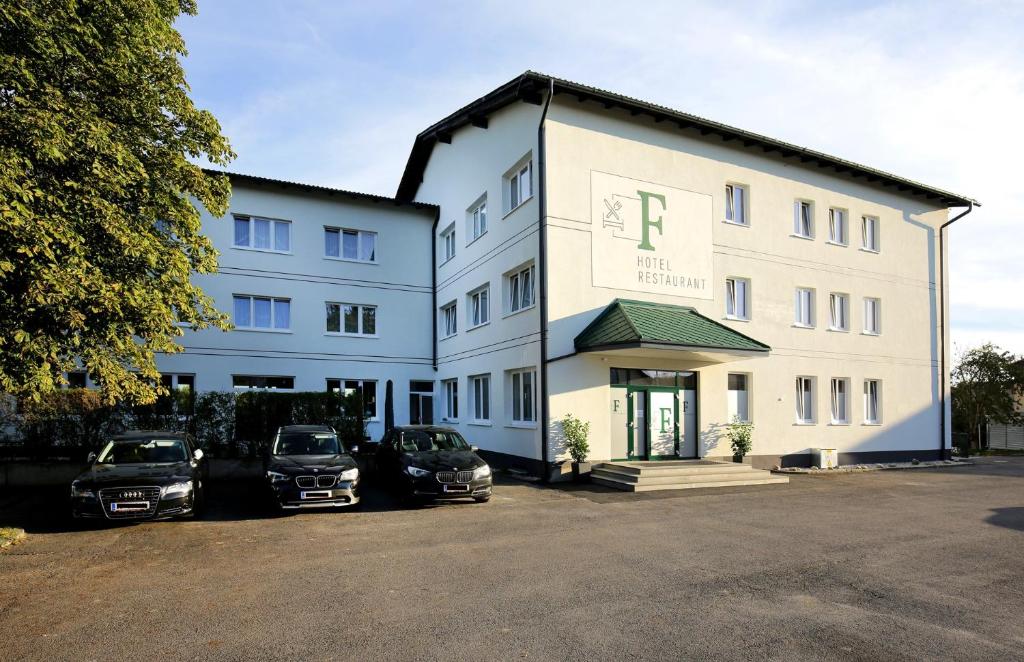 un edificio bianco con auto parcheggiate in un parcheggio di F Hotel a Hörsching