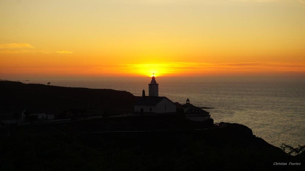 einen Leuchtturm auf einem Hügel mit Sonnenuntergang im Hintergrund in der Unterkunft EL CAMBARAL del PUERTO in Luarca