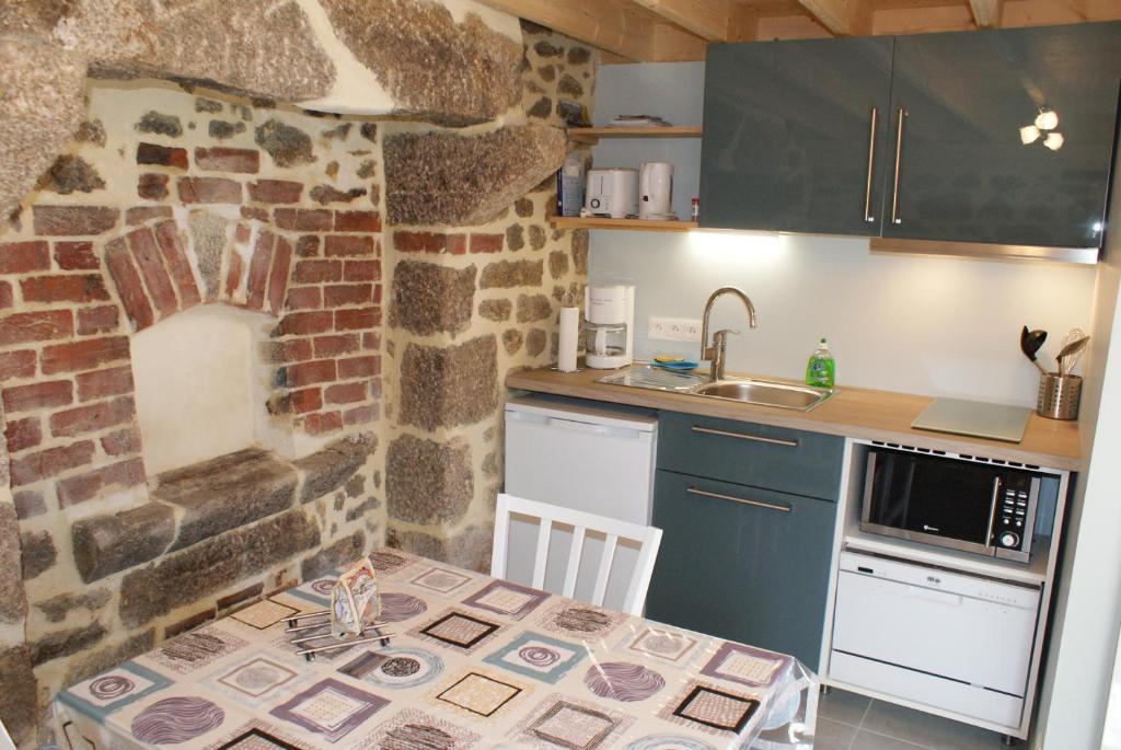 eine Küche mit einer Steinmauer, einem Tisch und einem Waschbecken in der Unterkunft La Boulangerie, charmant cocon pour déconnecter in Montfarville