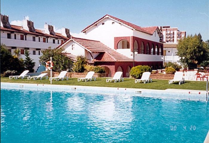 una piscina con sillas blancas y un edificio en Hotel Morales en San Clemente del Tuyú