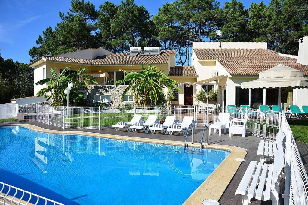 uma piscina com cadeiras brancas e uma casa em Villa Verdizela II em Carcereiro