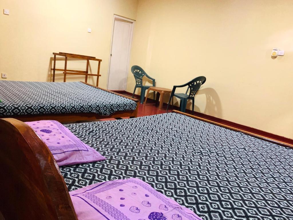 two beds in a room with two chairs and a table at New Jayani Guest Inn in Rakwana