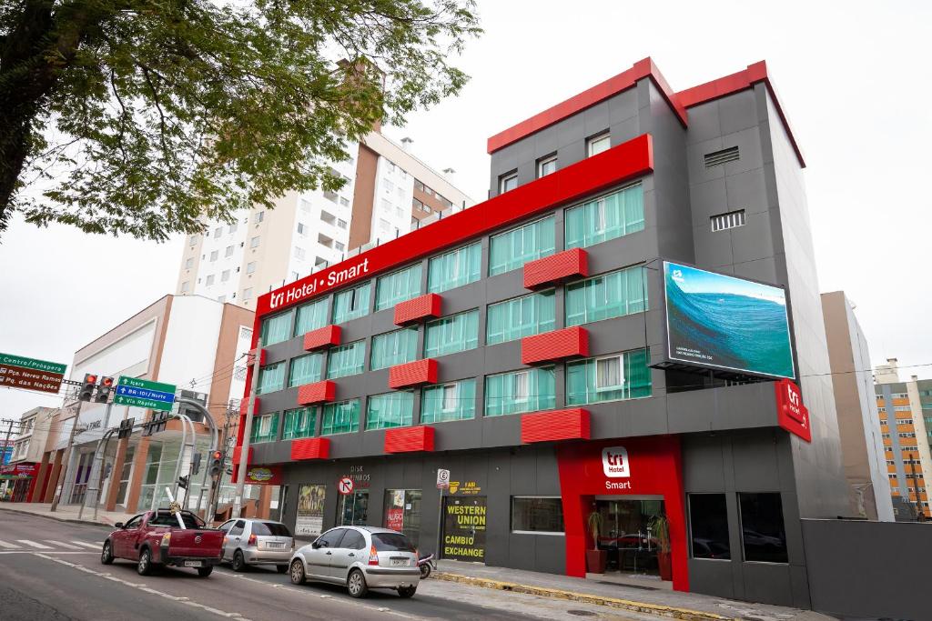 a red and gray building on a city street with cars at Tri Hotel Smart Criciuma in Criciúma