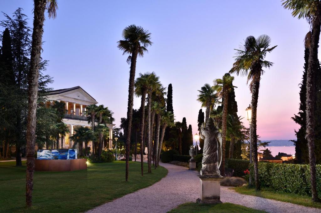 a statue in front of a house with palm trees at Villa Cortine Palace Hotel in Sirmione