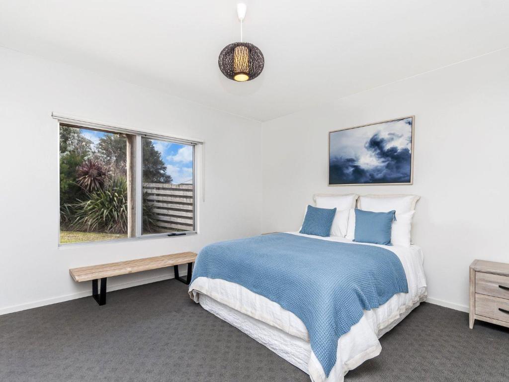 a white bedroom with a blue bed and a window at Escape 2 Brophy in Port Fairy