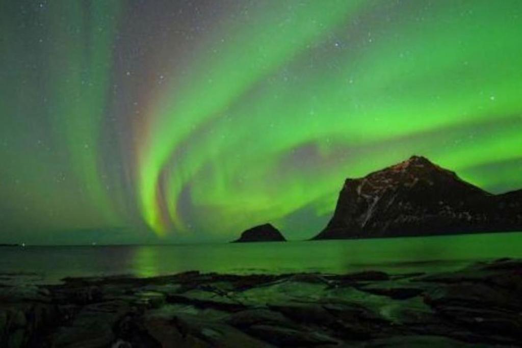 una aurora sobre las montañas y un cuerpo de agua en Northern Light Cabin Lofoten en Sennesvik