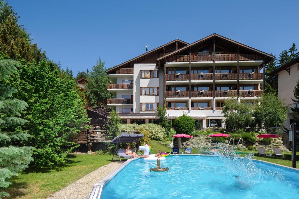 a hotel with a swimming pool in front of a building at Hotel La Prairie in Crans-Montana