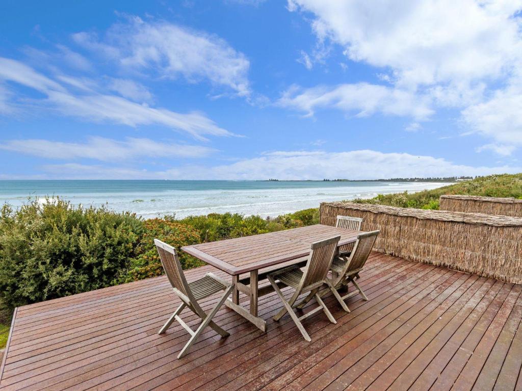 a wooden table and chairs on a deck with the beach at Rubys Beachfront in Port Fairy