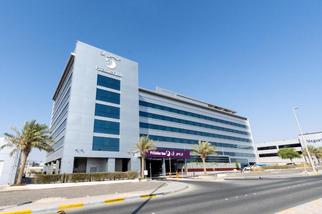 a large white building with palm trees in front of it at Premier Inn Abu Dhabi Airport Business Park in Abu Dhabi