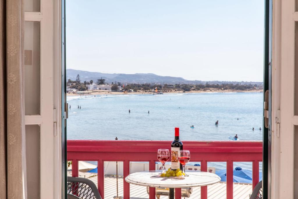 a table with a glass of wine and a view of the beach at Hotel Palatia in Naxos Chora