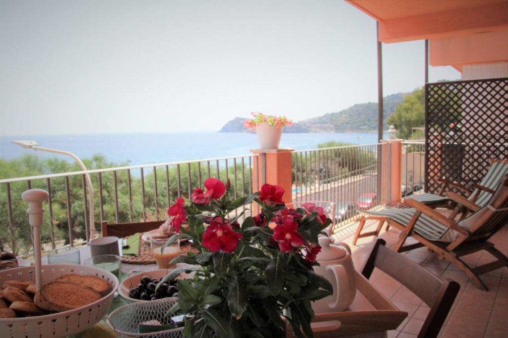 een tafel met rode bloemen op een balkon met uitzicht op de oceaan bij Poseidone Sea Apartment Taormina in Mazzeo