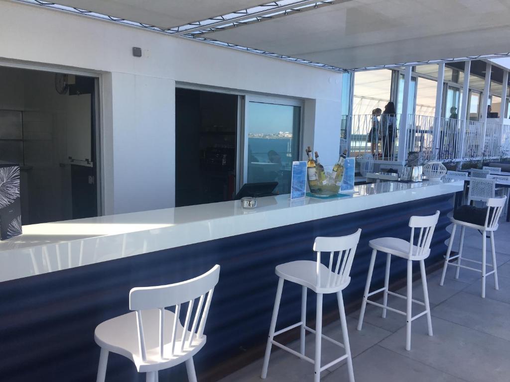 a bar with white stools in a room with windows at Hotel Baia in Cascais
