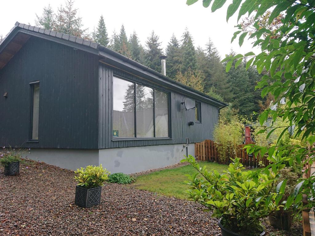 a black house with windows in a garden at Loch Ness Highland Cottages with partial Loch View in Invermoriston
