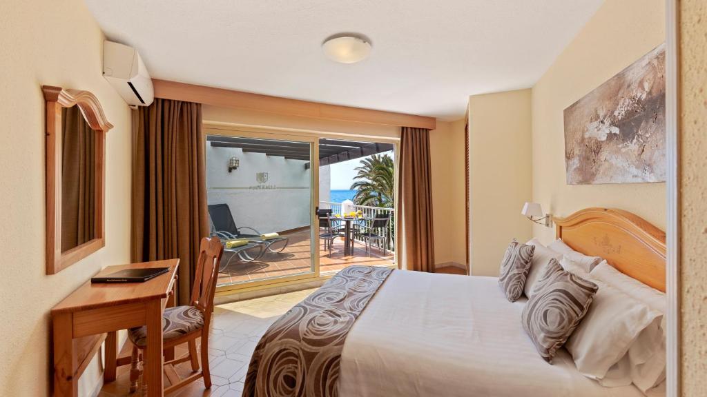 a bedroom with a bed and a desk and a balcony at Macdonald Leila Playa Resort in La Cala de Mijas