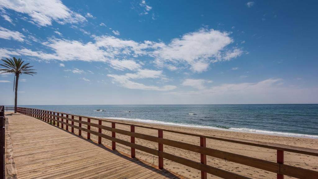 a wooden boardwalk leading to the beach with a palm tree at Macdonald Leila Playa Resort in La Cala de Mijas