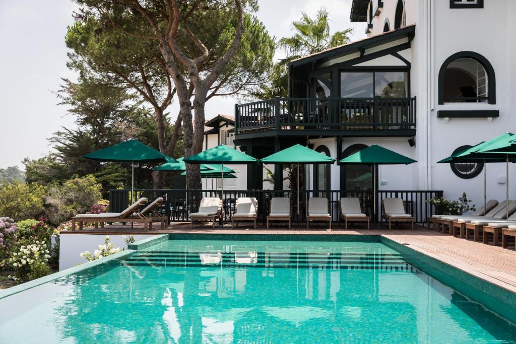 uma piscina com cadeiras e guarda-sóis ao lado de um edifício em Hôtel Les Hortensias du Lac em Hossegor