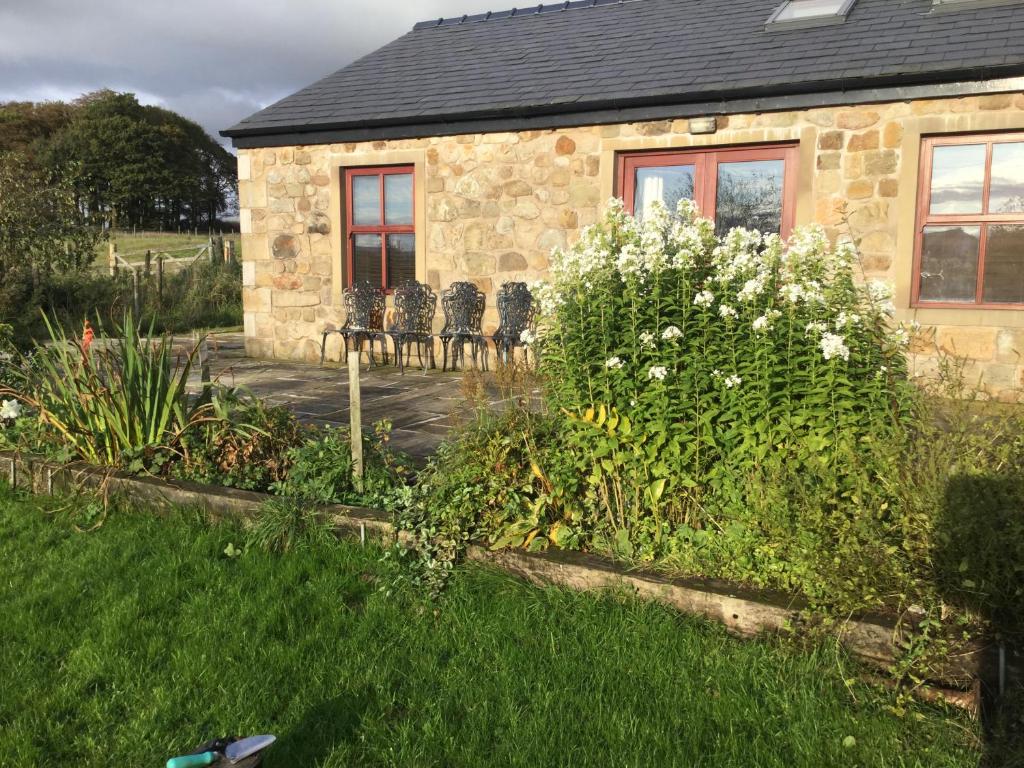 a stone house with chairs and flowers in a yard at Three Peaks View Cottage BD23 4SP in Wigglesworth