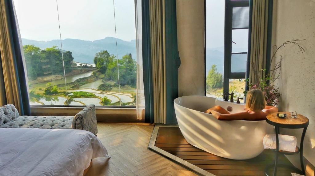 a woman sitting in a bathtub in front of a window at Twelve Manor Xiangdian Yuanyang Rice Terraces Retreat in Yuanyang