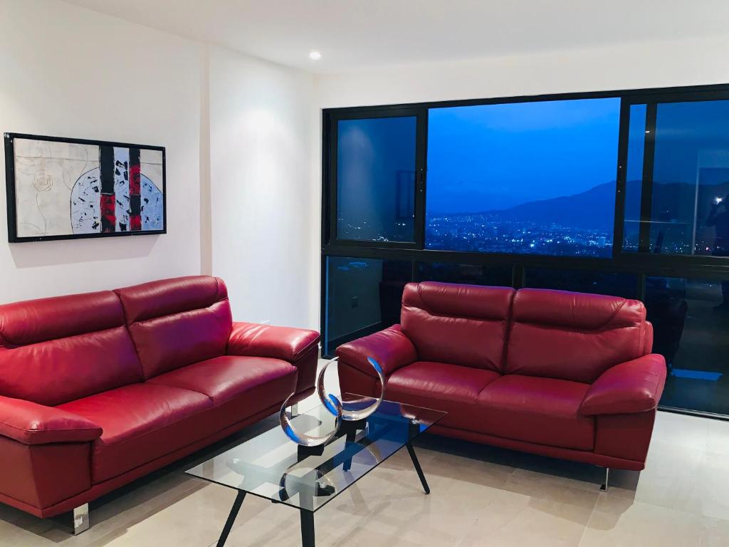 een woonkamer met rode lederen meubels en grote ramen bij APARTAMENTO CON LA MEJOR VISTA DE SAN SALVADOR in San Salvador
