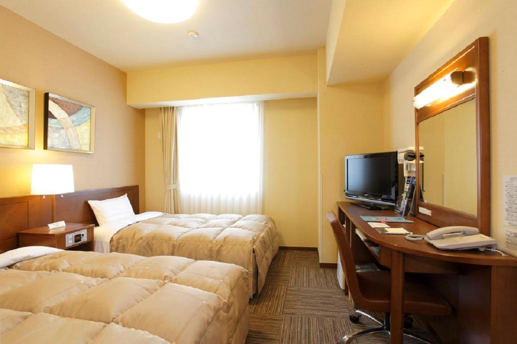 a hotel room with two beds and a desk with a computer at Hotel Route-Inn Ichinomiya Ekimae in Ichinomiya