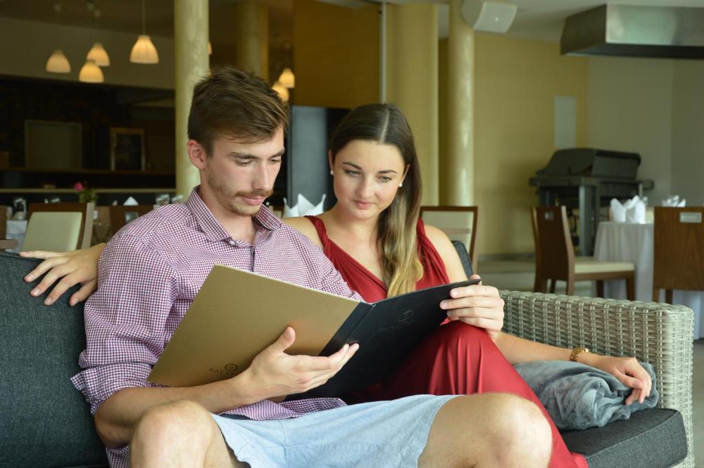 a man and woman sitting on a couch reading a book at Hotel Galatea in Mladá Boleslav