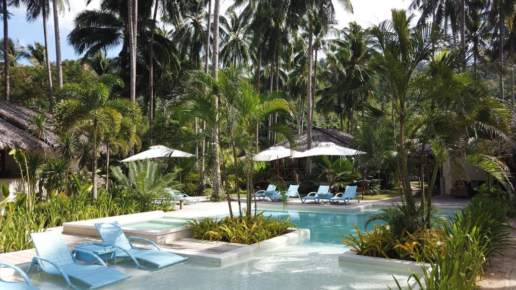 una piscina con sillas azules, sombrillas y palmeras en Mahogany Resort & Spa, en El Nido