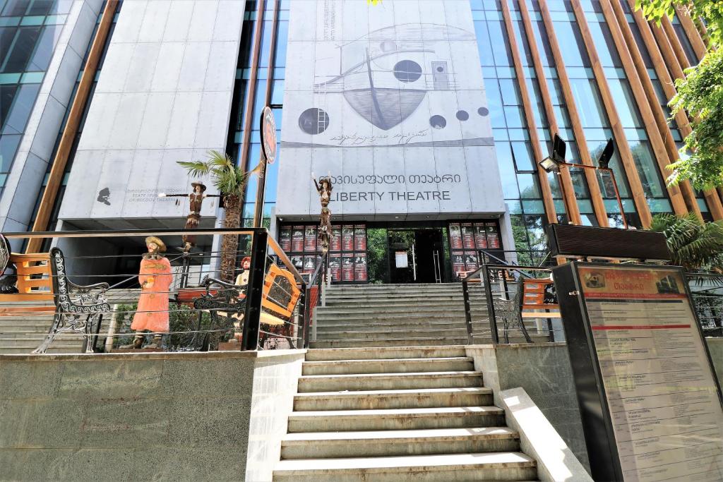 a woman in an orange dress walking up stairs in front of a building at Hotel Liberty Theatre in Tbilisi City