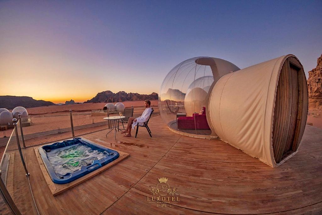 kobieta siedząca na krześle obok namiotu i wanny z hydromasażem w obiekcie Wadi Rum Bubble Luxotel w mieście Wadi Rum