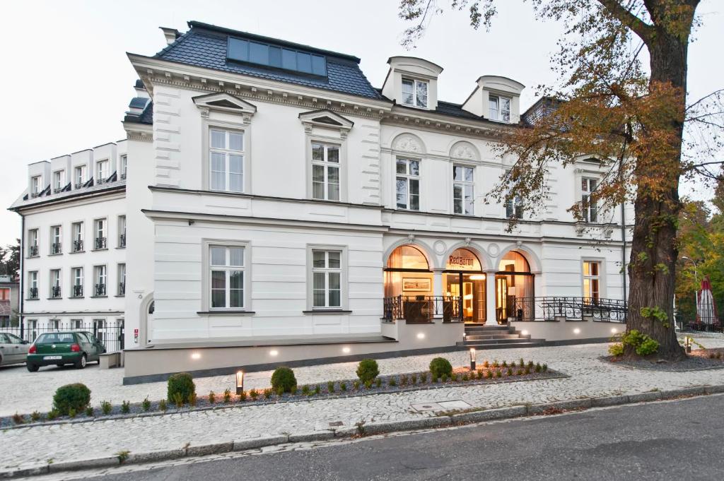 een wit huis met een boom ervoor bij Red Baron Hotel & Restaurant in Świdnica