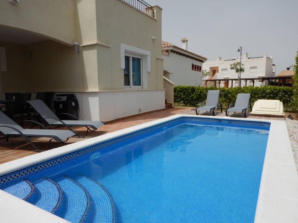 a swimming pool with chairs and a house at 2-bedroom Villa with pool in Torre-Pacheco