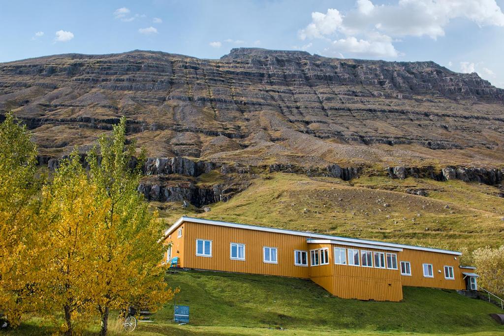 a building on a hill with a mountain in the background at Hafaldan HI Hostel - Harbour Building in Seyðisfjörður
