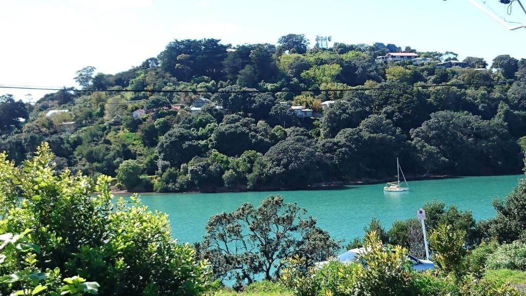 a sailboat in a lake with trees on a hill at Shelly Beach Studio, Waiheke Island in Auckland