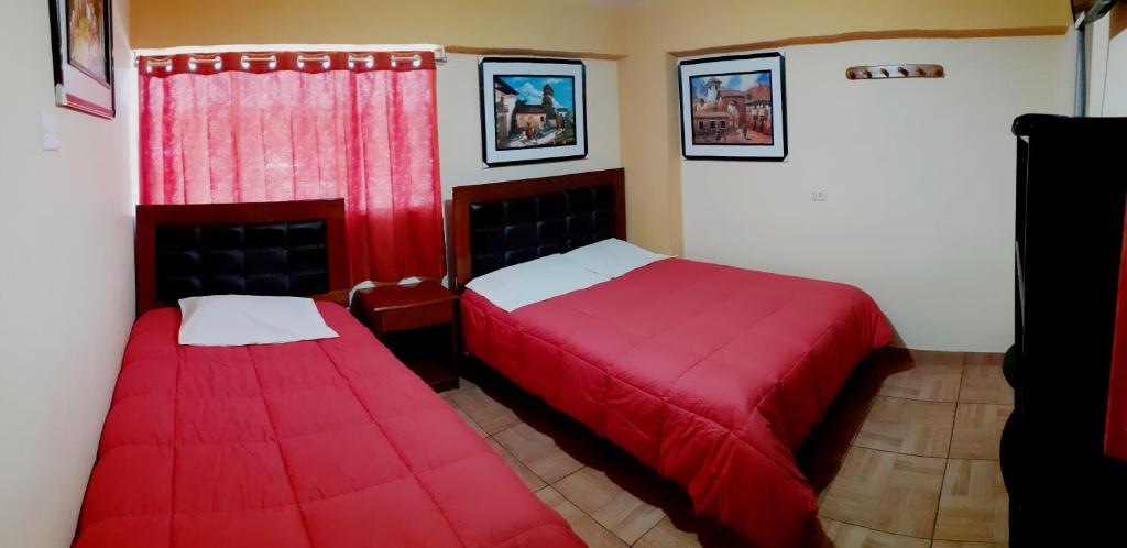 1 dormitorio con 2 camas con sábanas rojas y ventana en Hostal kuntur cusco, en Cusco