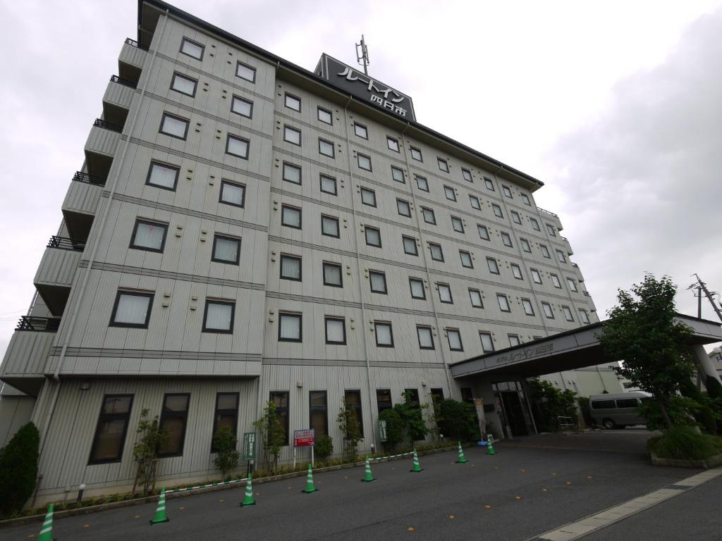 un grand bâtiment blanc avec des cônes verts devant lui dans l'établissement Hotel Route-Inn Yokkaichi, à Yokkaichi