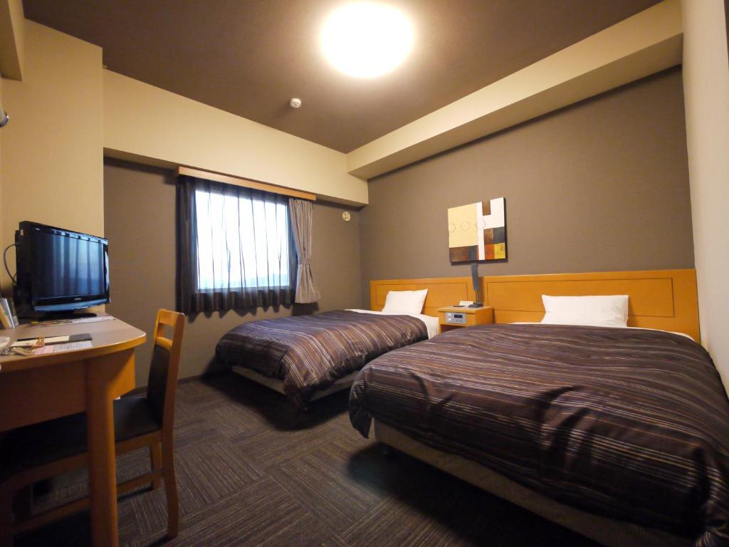 豊川市にあるホテルルートイン豊川インターのベッド2台、デスク、テレビが備わるホテルルームです。