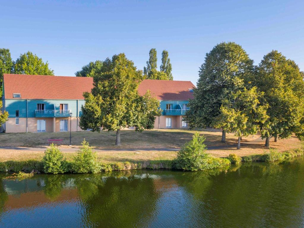 a house next to a lake with trees at ibis Styles Bourbon Lancy in Bourbon-Lancy