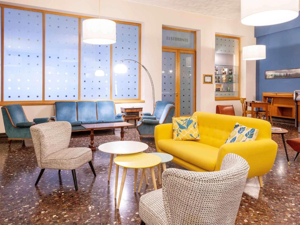 a lobby with a yellow couch and chairs and tables at ibis styles Trani in Trani